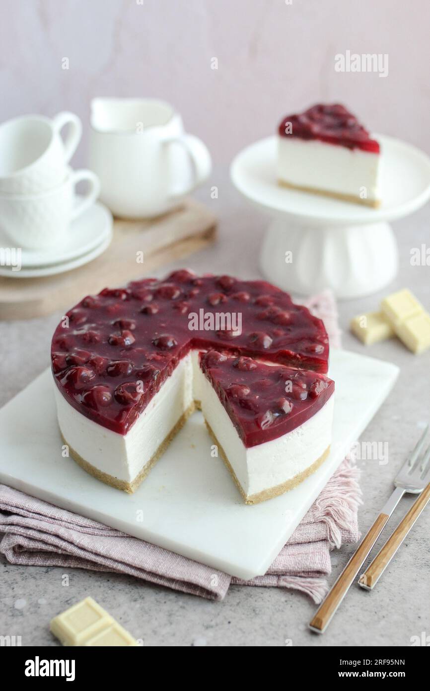 Gebackene weiße Schokolade und Kirschkäsekuchen auf einem weißen Teller. Weiße Kaffeetassen und rosafarbener Hintergrund. Stockfoto