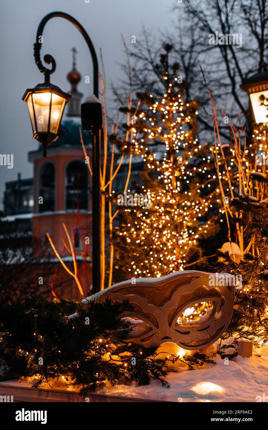 Theater-Karnevalsmaske, goldener Weihnachtsbaum und brennende Laterne in einer dekorierten Straße. Silvester Outdoor festliche magische Dekoration vertikal Stockfoto