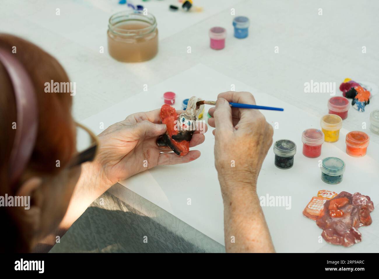 Alte Frau malt Gipsspielzeug, sitzt am Tisch. Nahaufnahme von Old Lady Hand. Zeichnen im Alter, Entwicklung kognitiver Fähigkeiten, seni-Prophylaxe Stockfoto