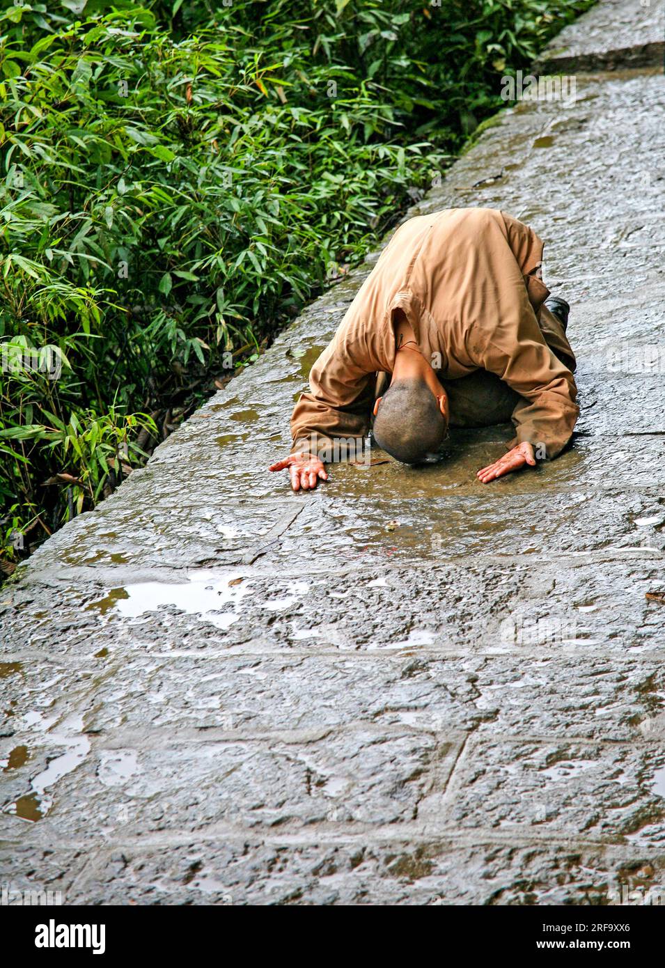 Buddhistischer Mönch prostruiert sich selbst mit nach oben gerichteten Palmen auf einem Steinweg, Emeishan, Provinz Sichuan, China Stockfoto