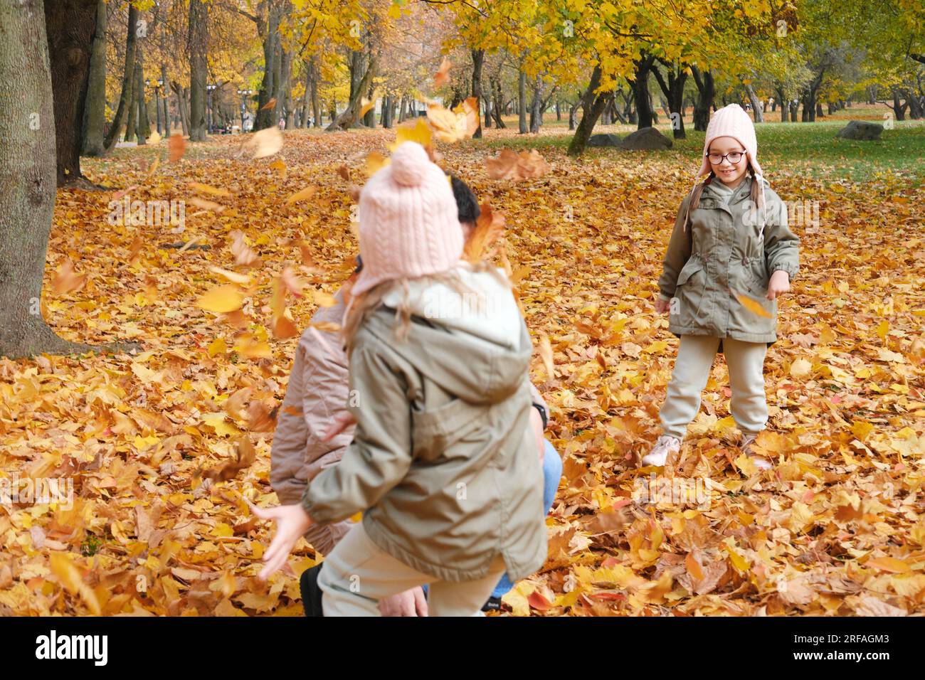 Vater und Töchter spielen im Herbstpark. Kinder werfen und werfen Blätter nach oben. Horizontales Foto Stockfoto