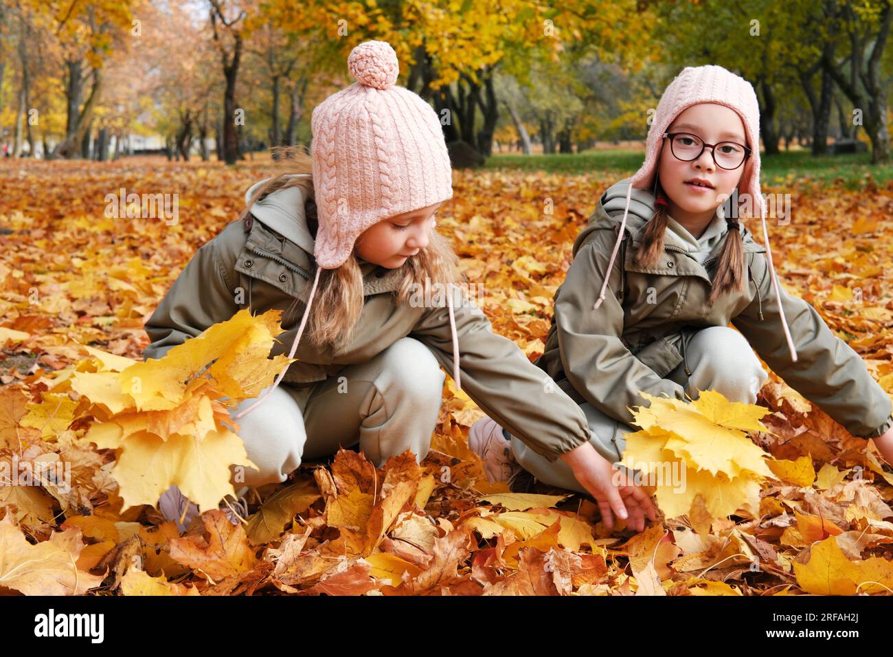 Zwei Zwillingsschwestern sammeln einen Strauß Herbstblätter im Park. Horizontales Foto Stockfoto
