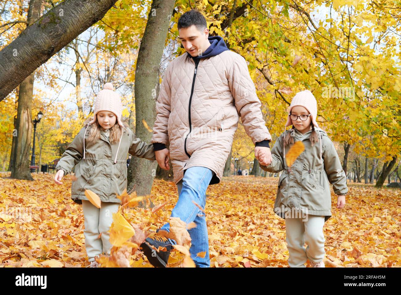 Dad geht mit seinen Zwillingstochter im Herbstpark spazieren. Die Familie tritt die Blätter hoch. Horizontales Foto Stockfoto