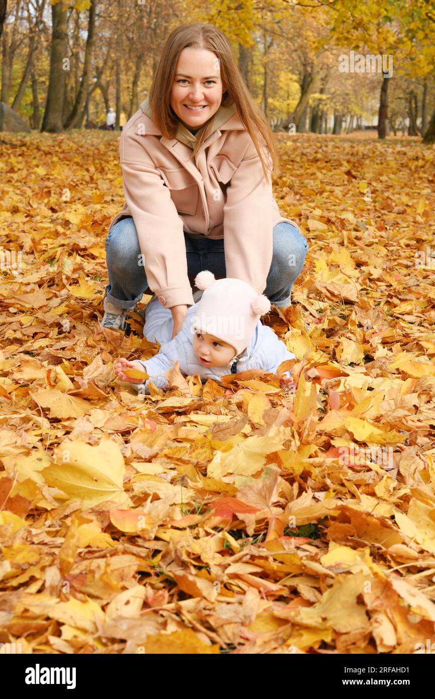 Mutter verbringt Zeit mit ihrer Tochter im Herbstpark. Mutter unterstützt ihre Tochter und hilft ihr, aufzustehen. Vertikales Foto Stockfoto