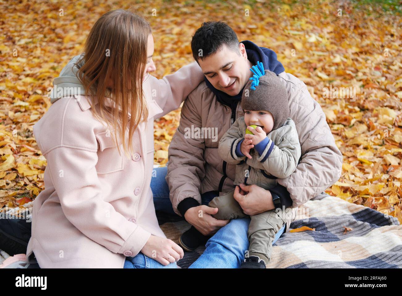 Familienwochenende. Junge Eltern und ihr kleiner Sohn verbringen Zeit zusammen im Herbstpark und sitzen auf einer Decke. Horizontales Foto Stockfoto