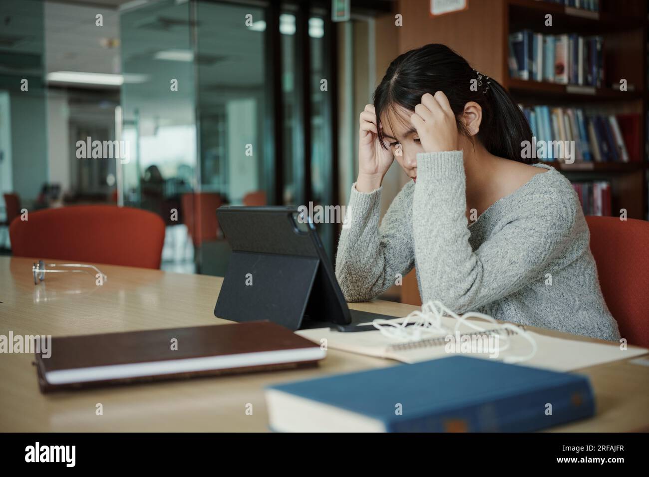 Asiatische Studentin liest Bücher in der Bibliothek an der Universität. Junge, stressmüde Mädchen haben Probleme beim Lernen. Traurigkeitskonzept Stockfoto