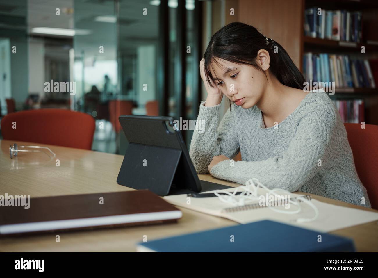 Asiatische Studentin liest Bücher in der Bibliothek an der Universität. Junge, stressmüde Mädchen haben Probleme beim Lernen. Traurigkeitskonzept Stockfoto