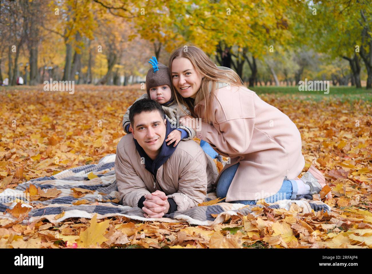 Familientag im Herbstpark. Eltern, deren Sohn in die Kamera schaut und lächelt. Horizontales Foto Stockfoto