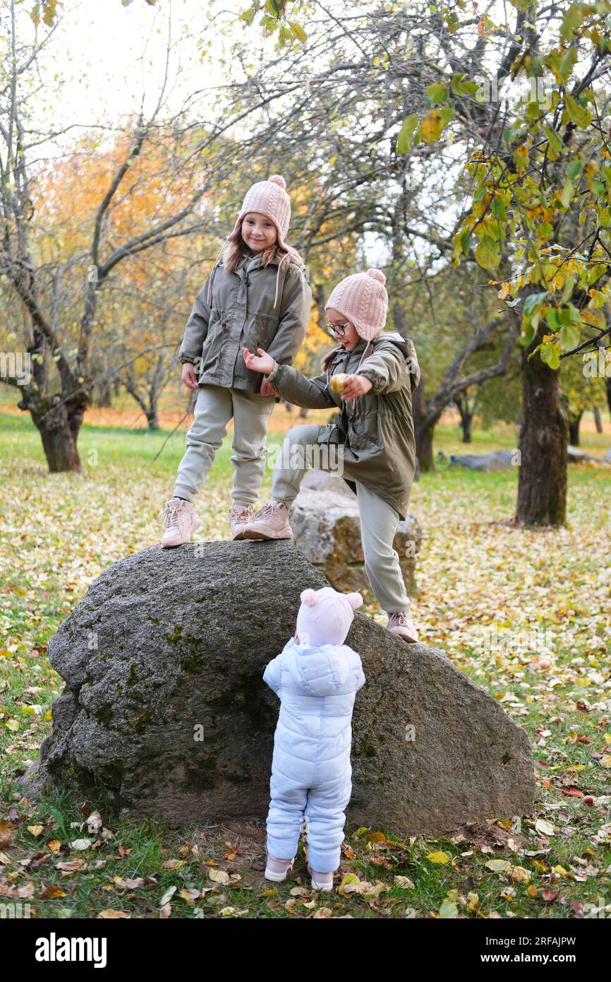 Kinder spielen im Apfelgarten im Herbst. Die Mädchen kletterten auf einen großen Felsen. Vertikales Foto Stockfoto