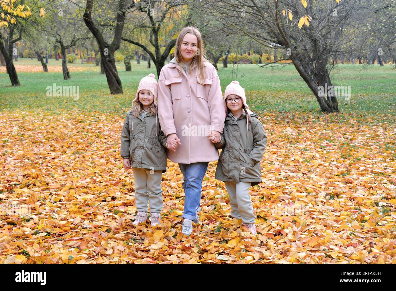 Im Herbstpark spielt die kaukasische Familie, die Mutter begrüßt zwei Zwillinge und lächelt, am aktiven Wochenende im Freien. Horizontales Foto Stockfoto