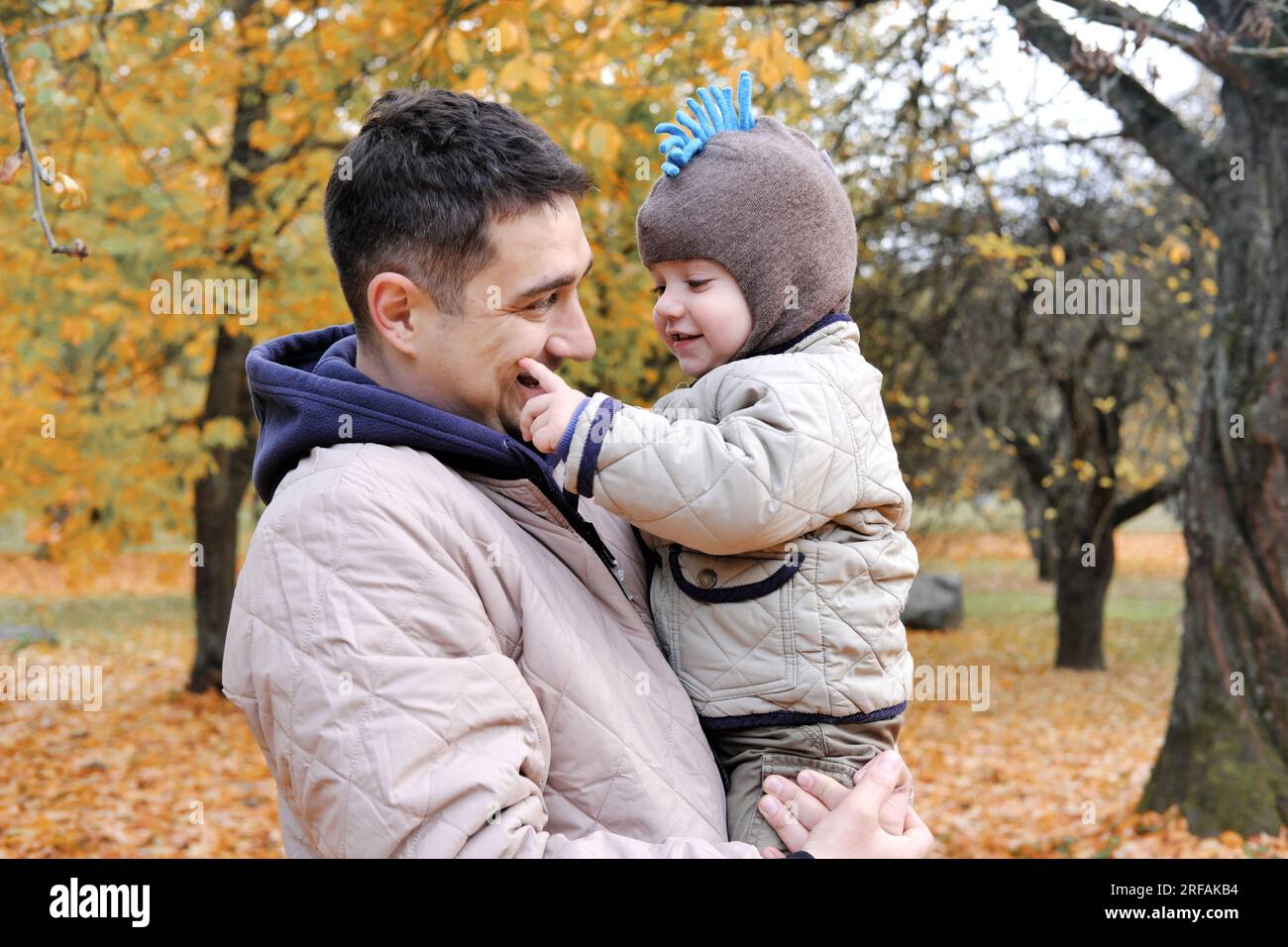 Dad und Sohn verbringen Zeit zusammen im Herbstpark. Vater hält seinen Sohn in den Armen. Horizontales Foto Stockfoto