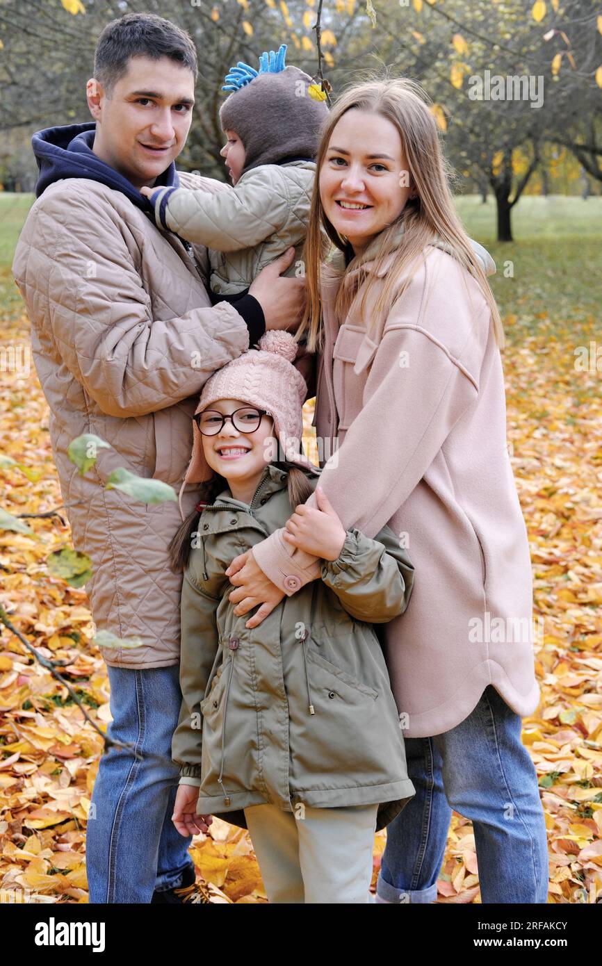 Eine vierköpfige Familie hat Spaß im Herbstpark. Die Familie schaut in die Kamera und lächelt. Vertikales Foto Stockfoto