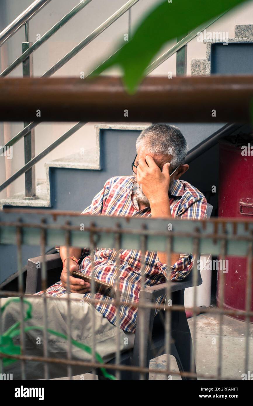Oktober 14. 2022 Uttarakhand, Indien. Ein älterer Inder im Ruhestand genießt Inhalte auf seinem Smartphone im ruhigen Hinterhof. Technologie für Leisu Stockfoto
