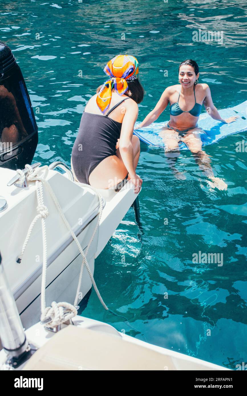 Zwei junge Frauen, die sich unterhalten, sitzen auf einem Boot und auf einem Floß, im Meer, und genießen den Sommer Stockfoto