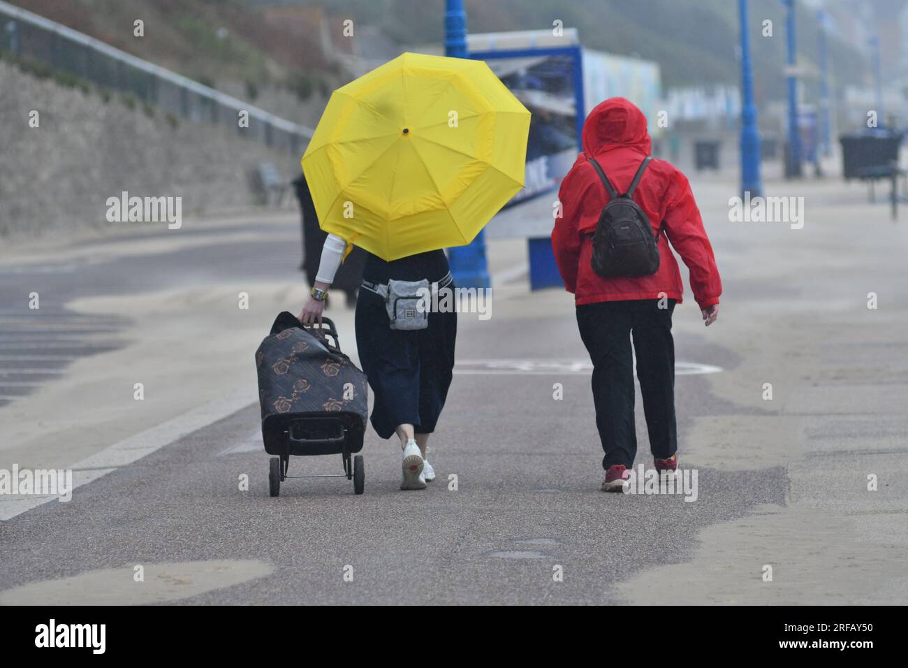 Zwei Frauen, die am Meer spazieren, Bournemouth, Dorset, England, Großbritannien, 2. August 2023, Wetter. Wild und windig mit starken Regenschauern, während der nasse Sommer weitergeht. An der Südküste gibt es eine Wetterwarnung für starke Winde. Kredit: Paul Biggins/Alamy Live News Stockfoto