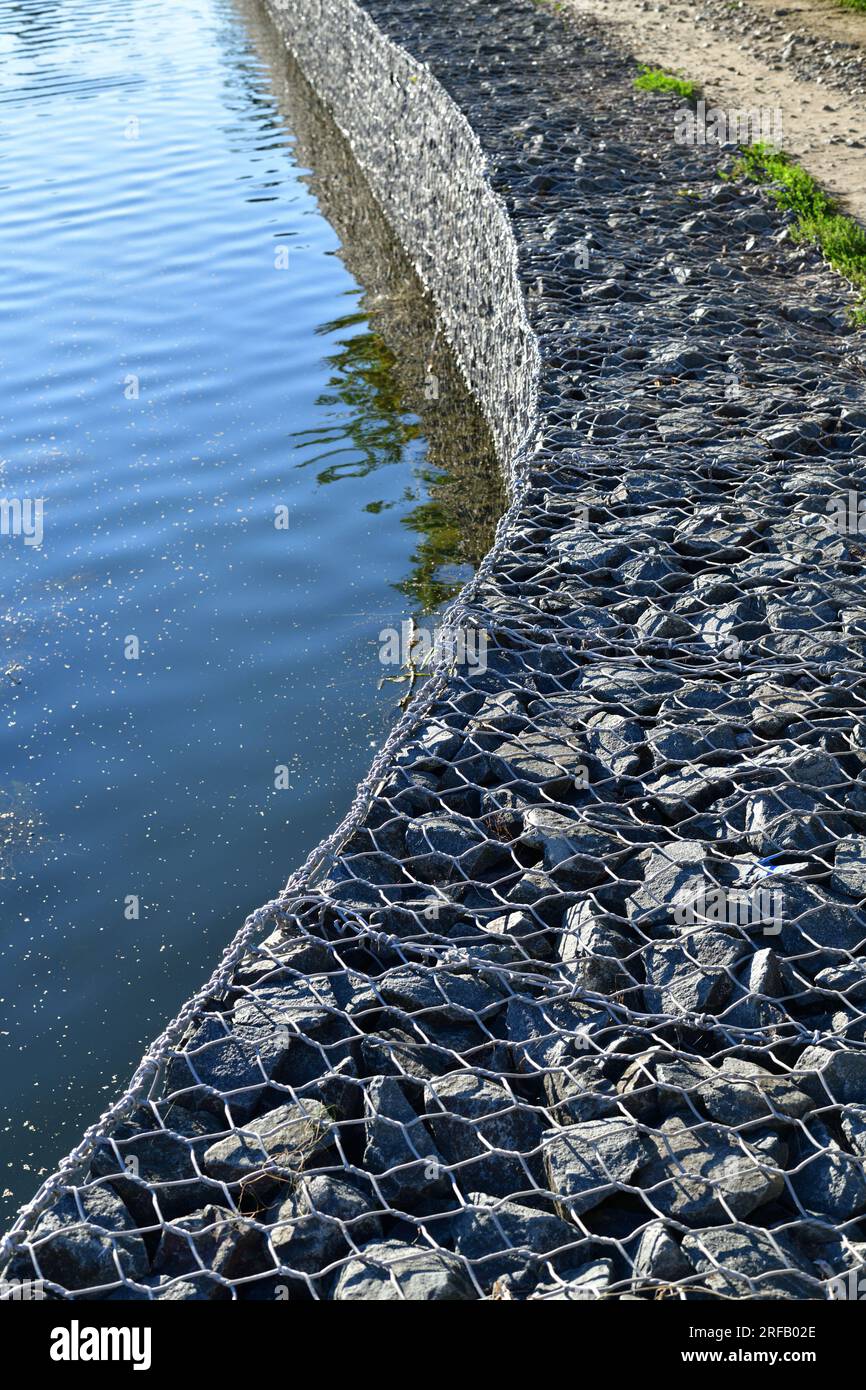 Verstärkung des Ufers des Reservoirs mit Steinen unter einem Metallgitter Stockfoto