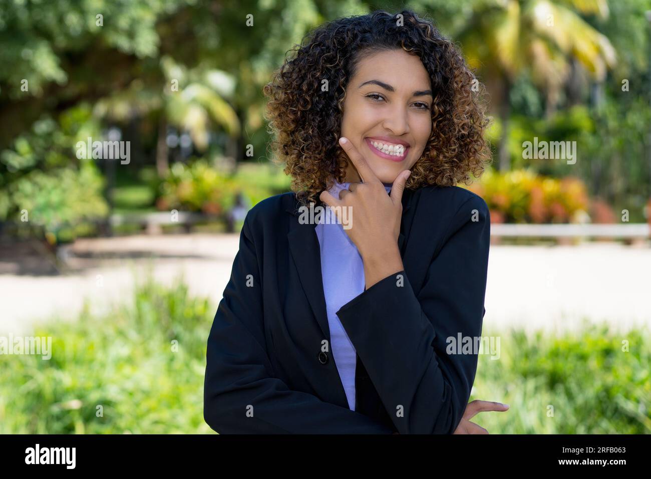 Lachende lateinamerikanische Geschäftsfrau mit blauem Blazer draußen in der Stadt im Sommer Stockfoto