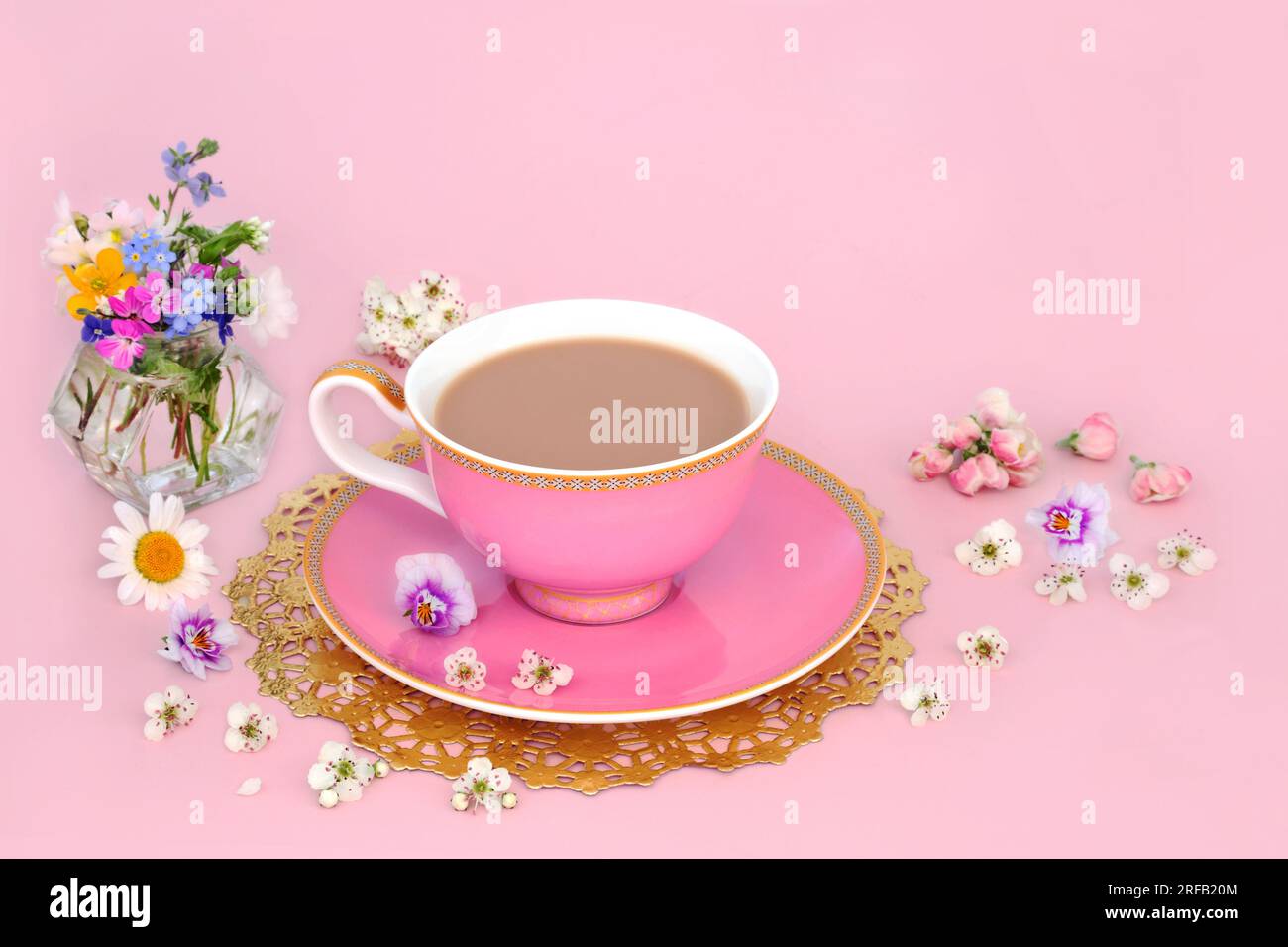 Nachmittagstee mit Frühlingsblumen und Wildblumen in einer Vase und verstreut. Luxuriöse Teetasse auf goldenem Teig auf pinkfarbenem Hintergrund. Stockfoto