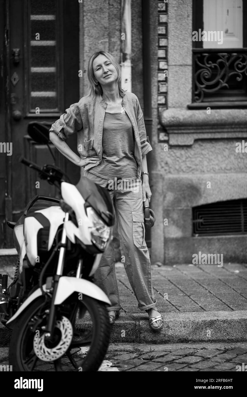 Eine Frau mit Kopfhörern in der Hand steht neben einem Motorrad. Schwarzweißfoto. Stockfoto