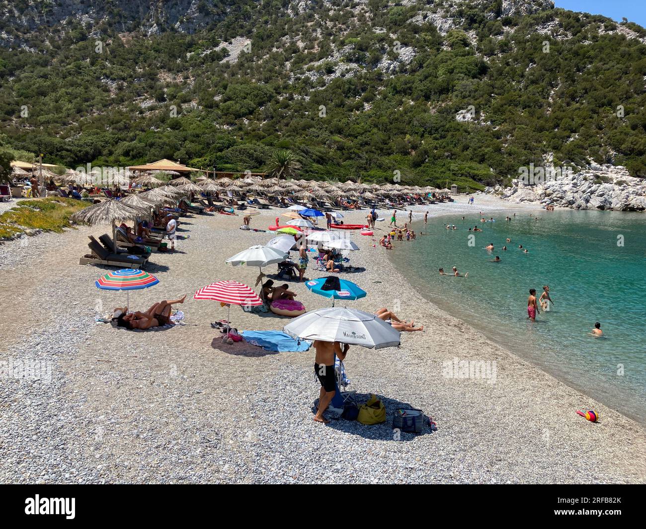 Skopelos, Griechenland. 02. Aug. 2023. Die Leute verbringen den heißen Sommertag an einem Strand auf der Sporades Insel Skopelos. Einige sitzen unter ihren eigenen bunten Schirmen, andere unter Strohschirmen, die gemietet werden können. Das ist auch nach griechischem Recht richtig, das besagt, dass die Bürger freien, ungehinderten Zugang zu den auf jeden Fall öffentlichen Stränden haben müssen. Das griechische Gesetz erkennt keine privaten Strände an. Kredit: Alexia Angelopoulou/dpa/Alamy Live News Stockfoto