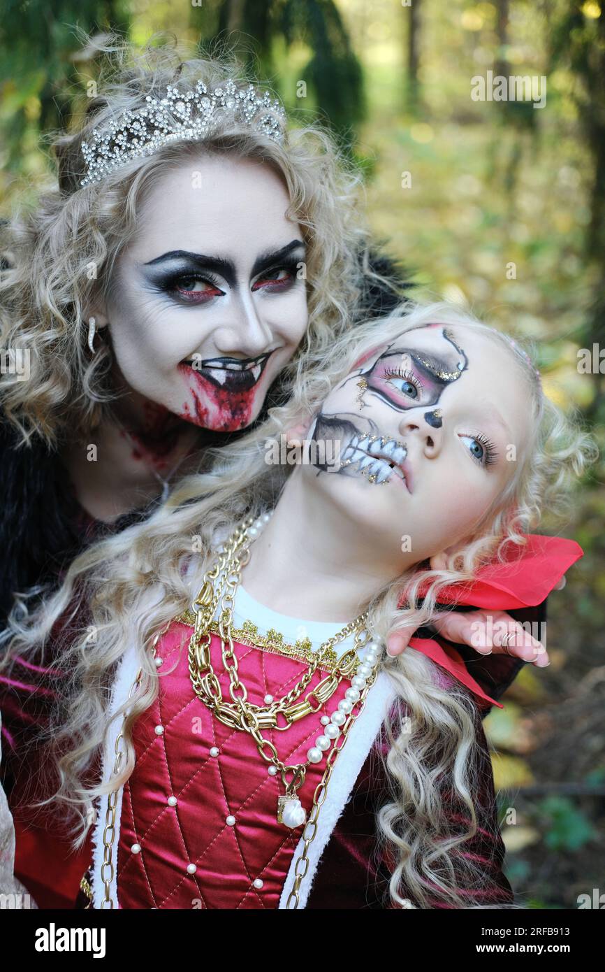 Eine Frau in Form eines Vampirs oder einer Zauberin lächelt und beißt eine Prinzessin in märchenhaftem Make-up und mittelalterlichem Kleid. Bild für Hallowe Stockfoto