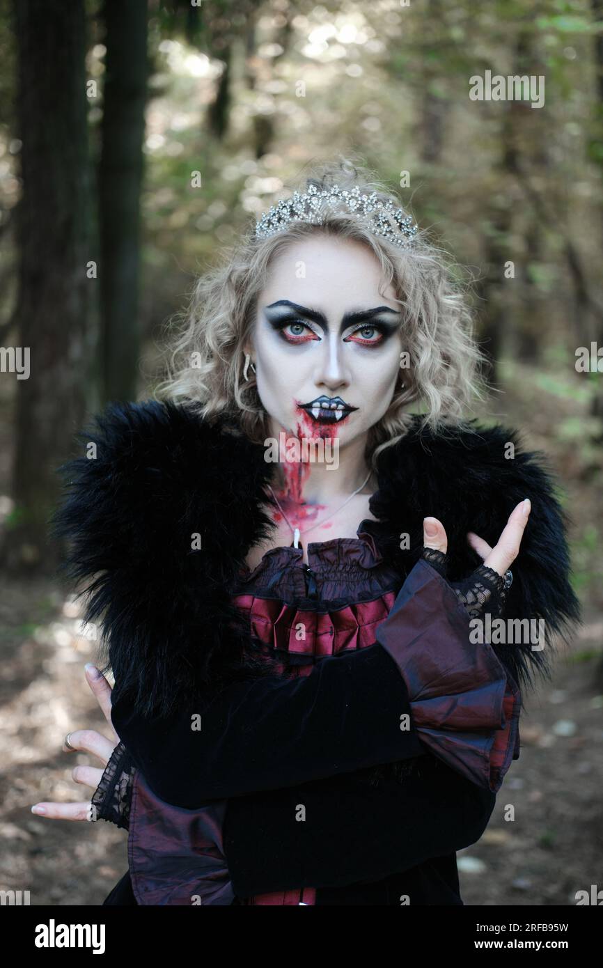 Eine Frau in Form eines Vampirs oder einer Hexe mit Make-up im Gesicht posiert für die Kamera im Wald. Vertikales Foto Stockfoto