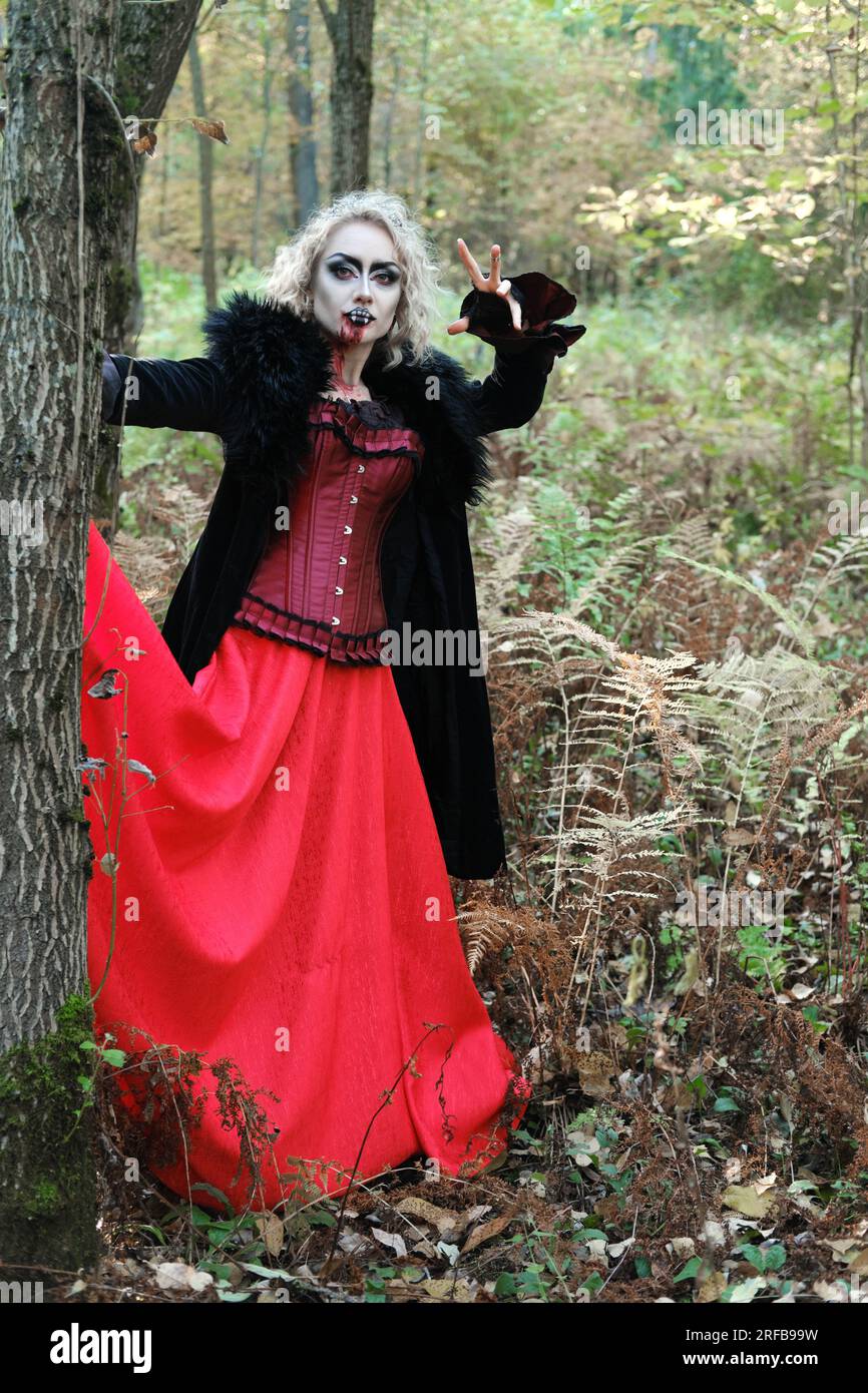 Eine Frau im Bild eines Vampirs oder einer Hexe mit weißer Schminke und in einem mittelalterlichen Kleid posiert im Wald vor der Kamera. Vertikales Foto Stockfoto