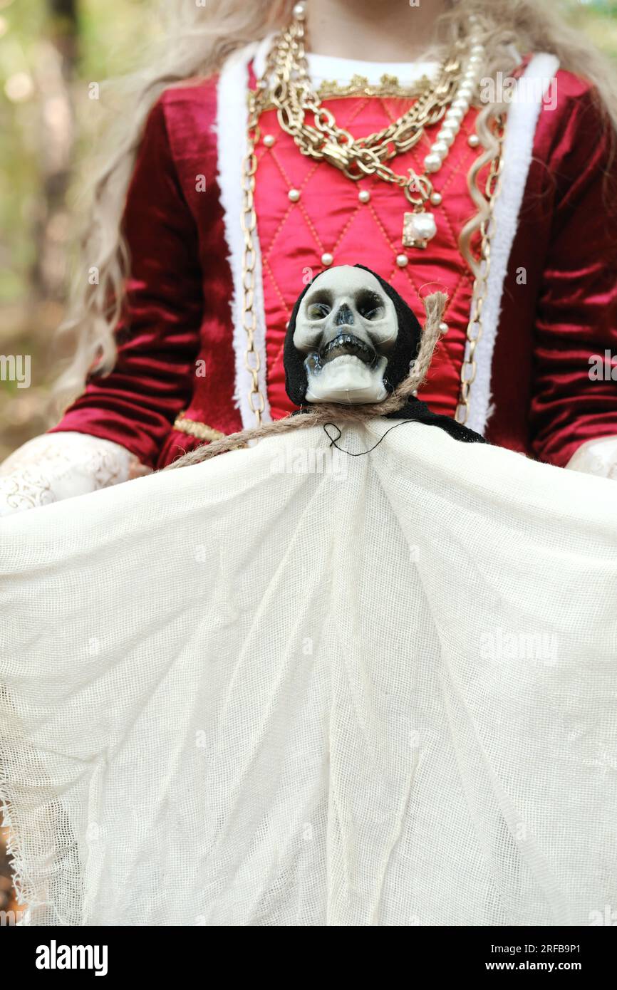 Ein Mädchen in einem mittelalterlichen Kleid hält eine Puppe in Form des Todes mit einem Skelettkopf. Vertikales Foto Stockfoto