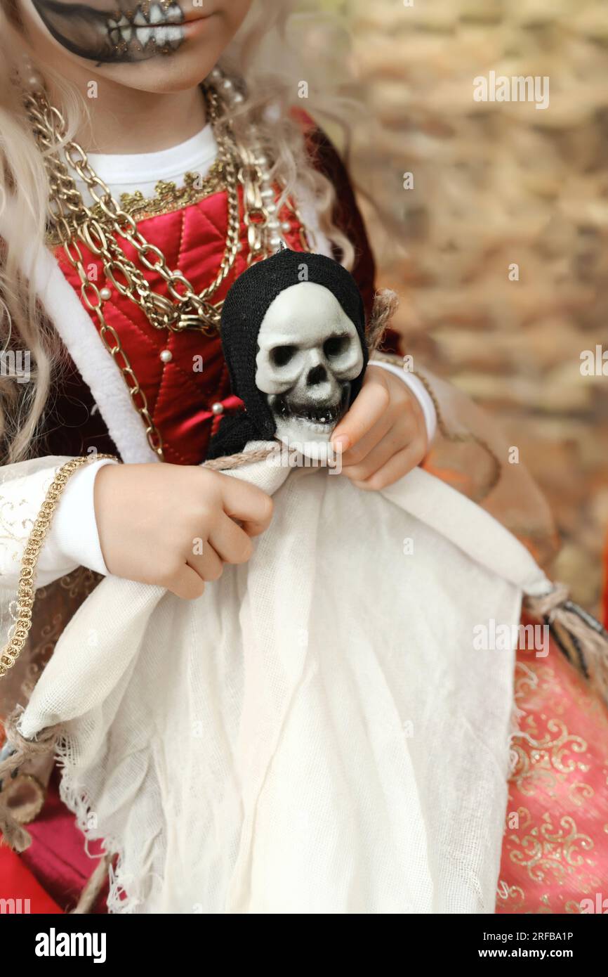 Ein Mädchen in einem mittelalterlichen Kleid hält eine Puppe in Form des Todes mit einem Skelettkopf. Vertikales Foto Stockfoto