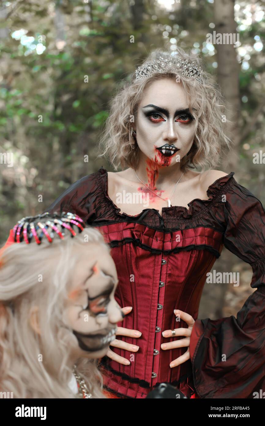 Eine Frau in Form eines Vampirs oder einer Zauberin schaut in die Kamera. Ein Mädchen in Form einer toten Prinzessin sitzt neben ihr. Bild für Halloween. Mo Stockfoto