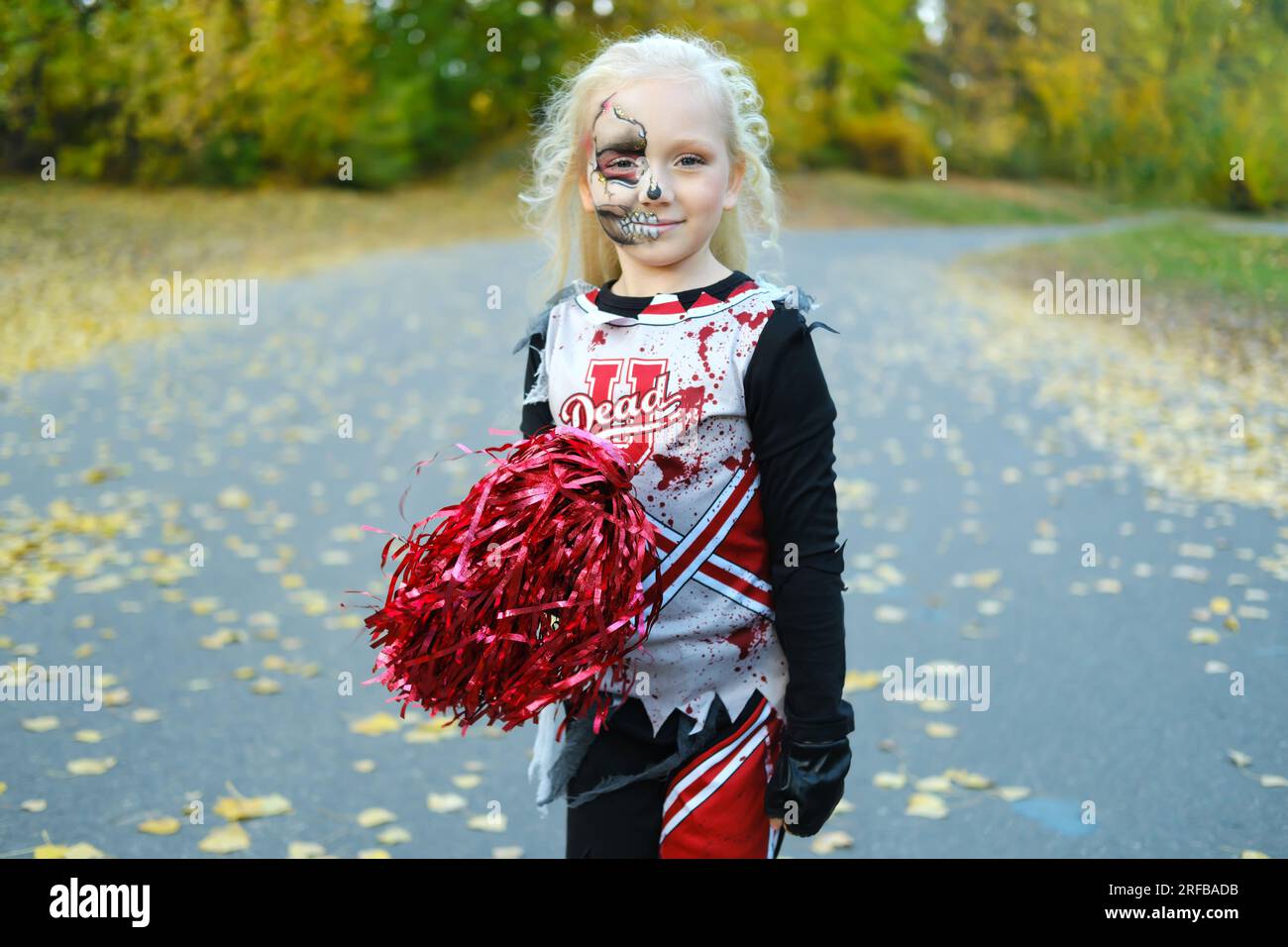 Ein Mädchen in einem Cheerleader-Kostüm und Halbgesichtsschminke in Form eines Skeletts feiert Halloween. Horizontales Foto Stockfoto