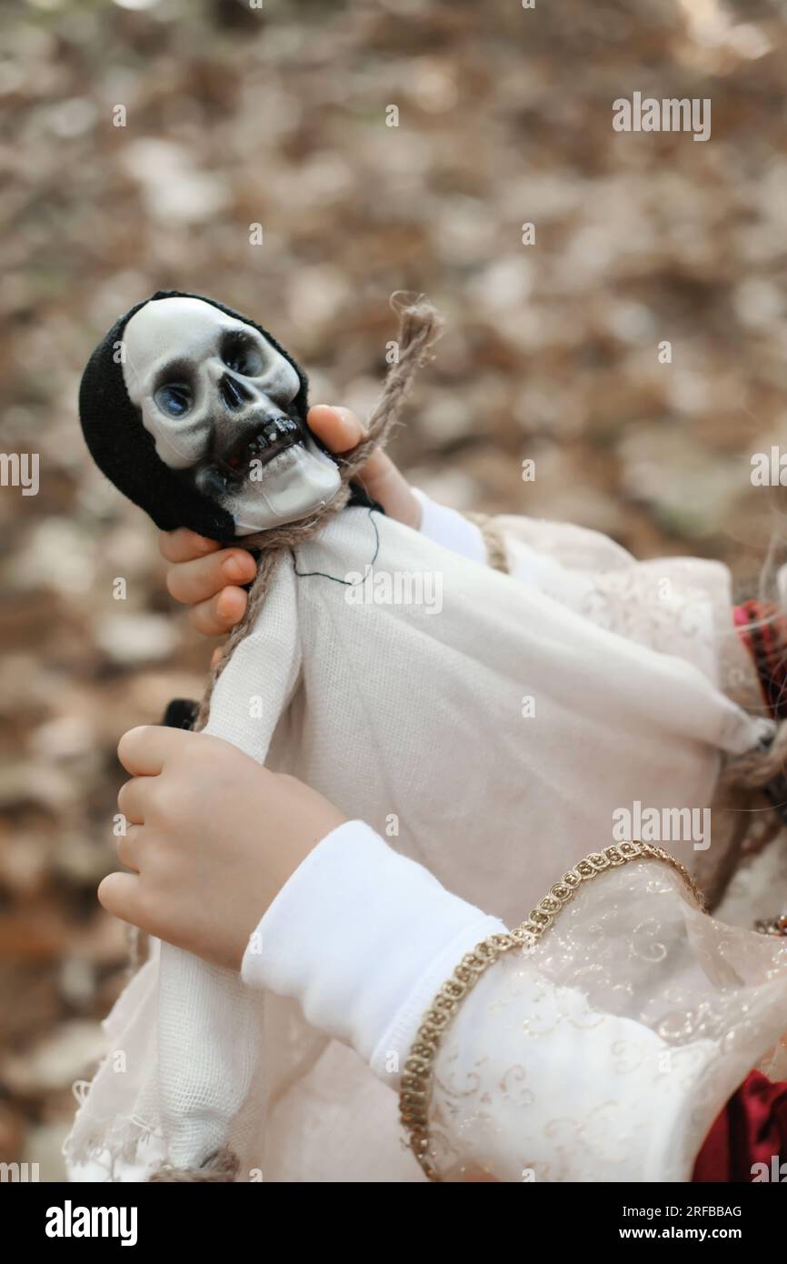 Ein Mädchen, das eine Puppe in Todesform hält, mit einem Skelettkopf. Vertikales Foto Stockfoto