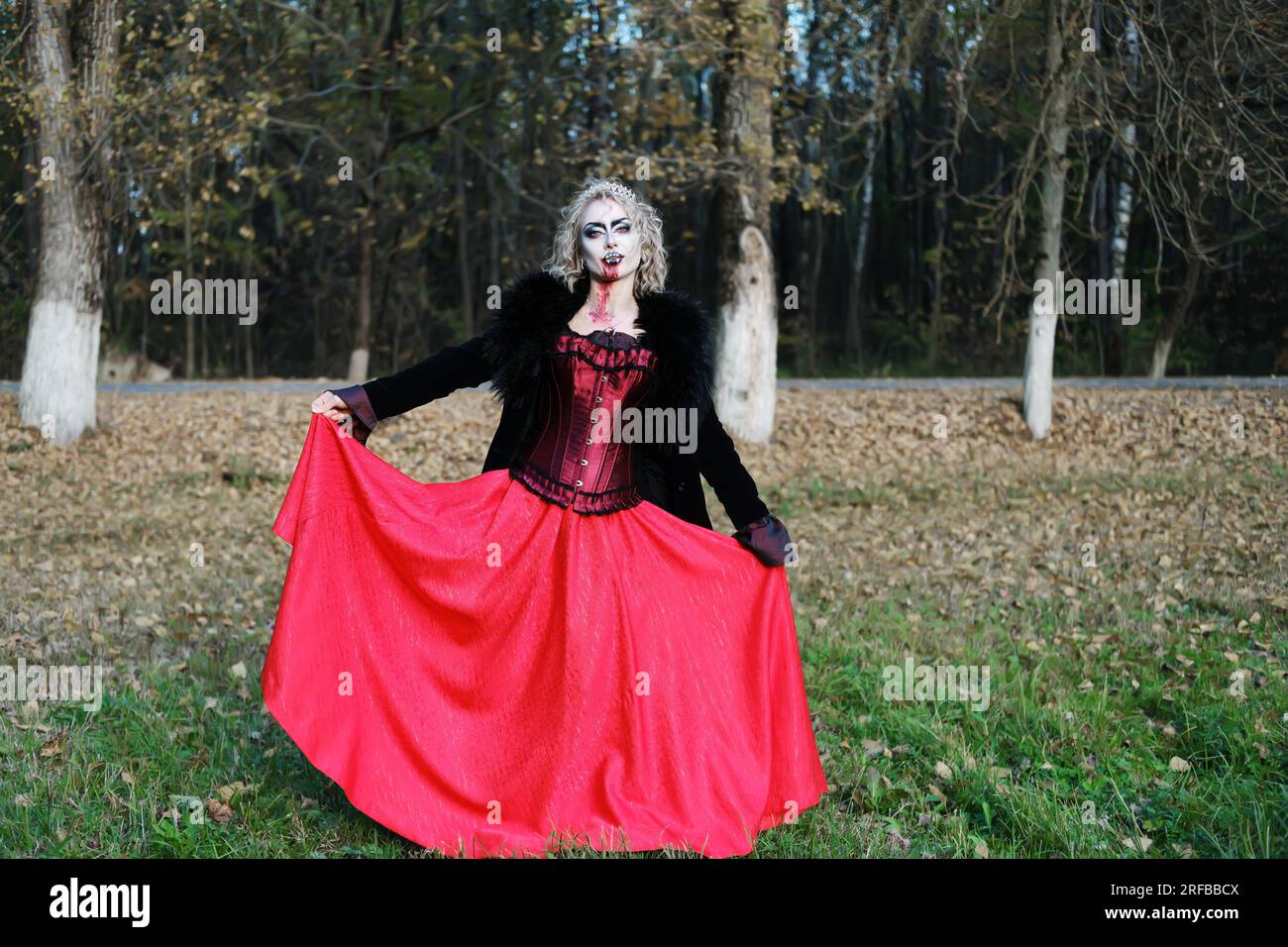 Eine Frau im Bild eines Vampirs oder einer Hexe mit weißer Schminke und in einem mittelalterlichen Kleid posiert im Wald vor der Kamera. Horizontales Foto Stockfoto