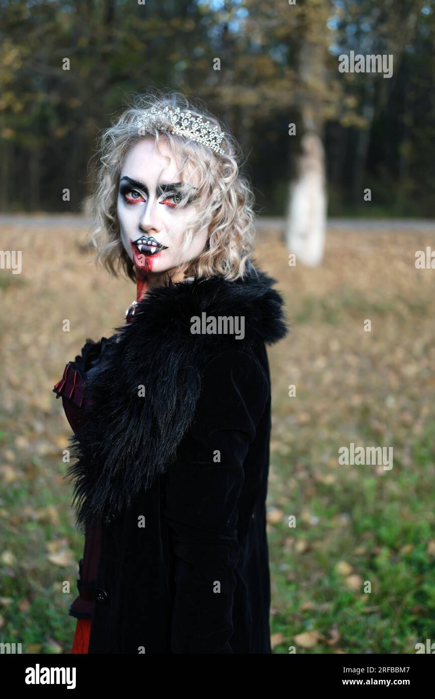 Eine Frau in Form eines Vampirs oder einer Hexe mit weißem Make-up im Gesicht. Das Blut tropft dem Vampir ins Kinn. Eine Frau, die in die Kamera schaut. Vertikale Pho Stockfoto