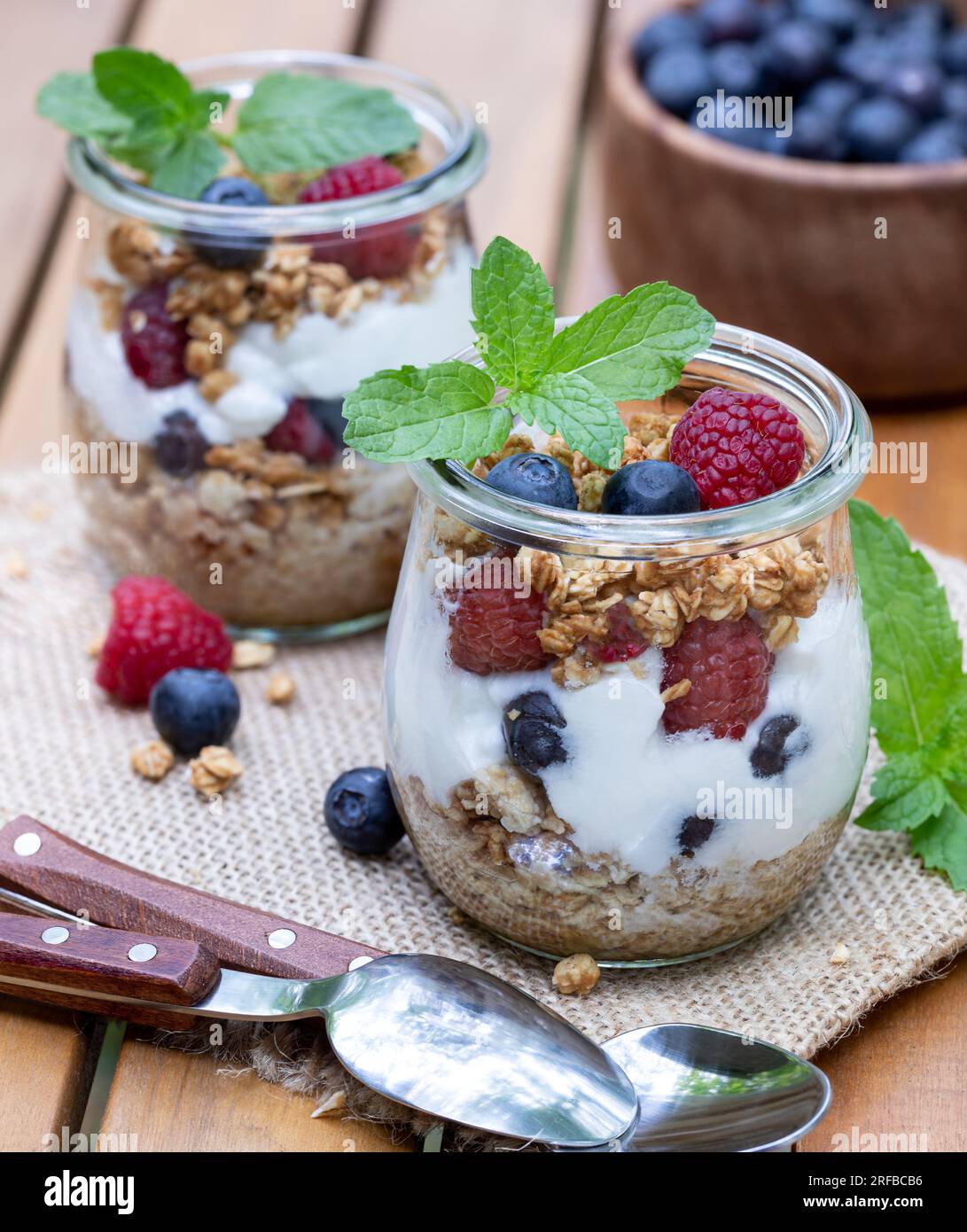Joghurtparfait mit Müsli, Heidelbeeren und Himbeeren, garniert mit Minze im Freien auf einem hölzernen Terrassentisch Stockfoto