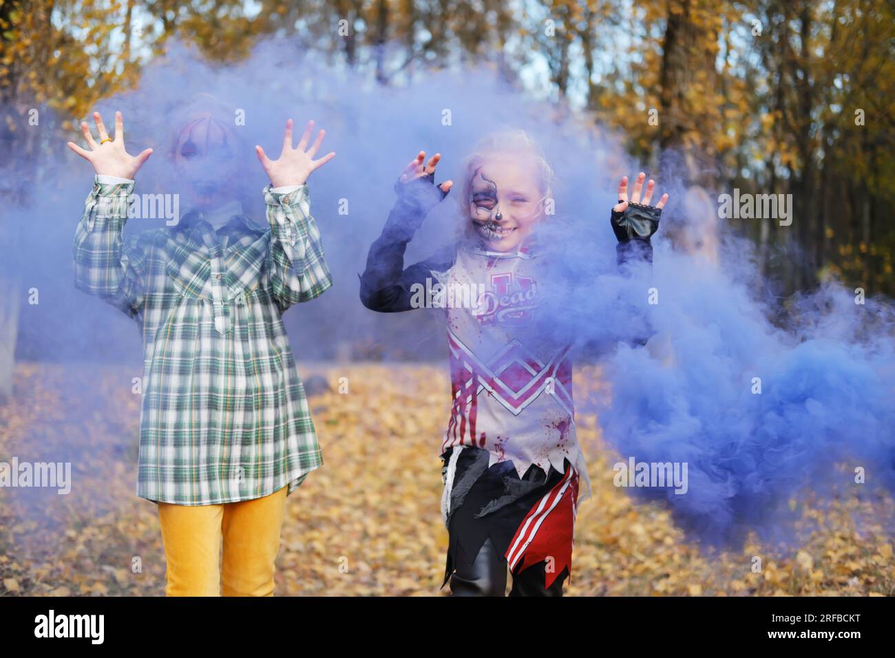 Zwei Kinder Mädchen Mädchen Freundinnen in Halloween-Kostümen und mit Make-up machen erschreckende Grimaces vor dem Hintergrund von Herbstblättern und lila schminke Stockfoto
