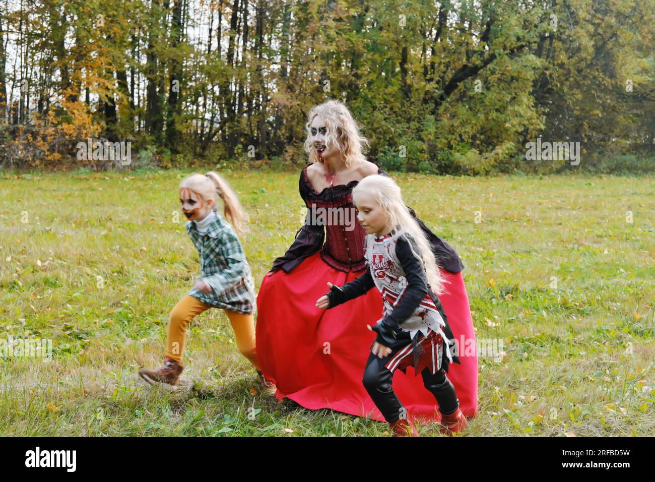 Die Familie feiert Halloween. Mom in Form eines Vampirs, Mädchen in Form einer Cheerleaderin und eines Kürbis. Mom spielt mit ihren Töchtern. Horizont Stockfoto