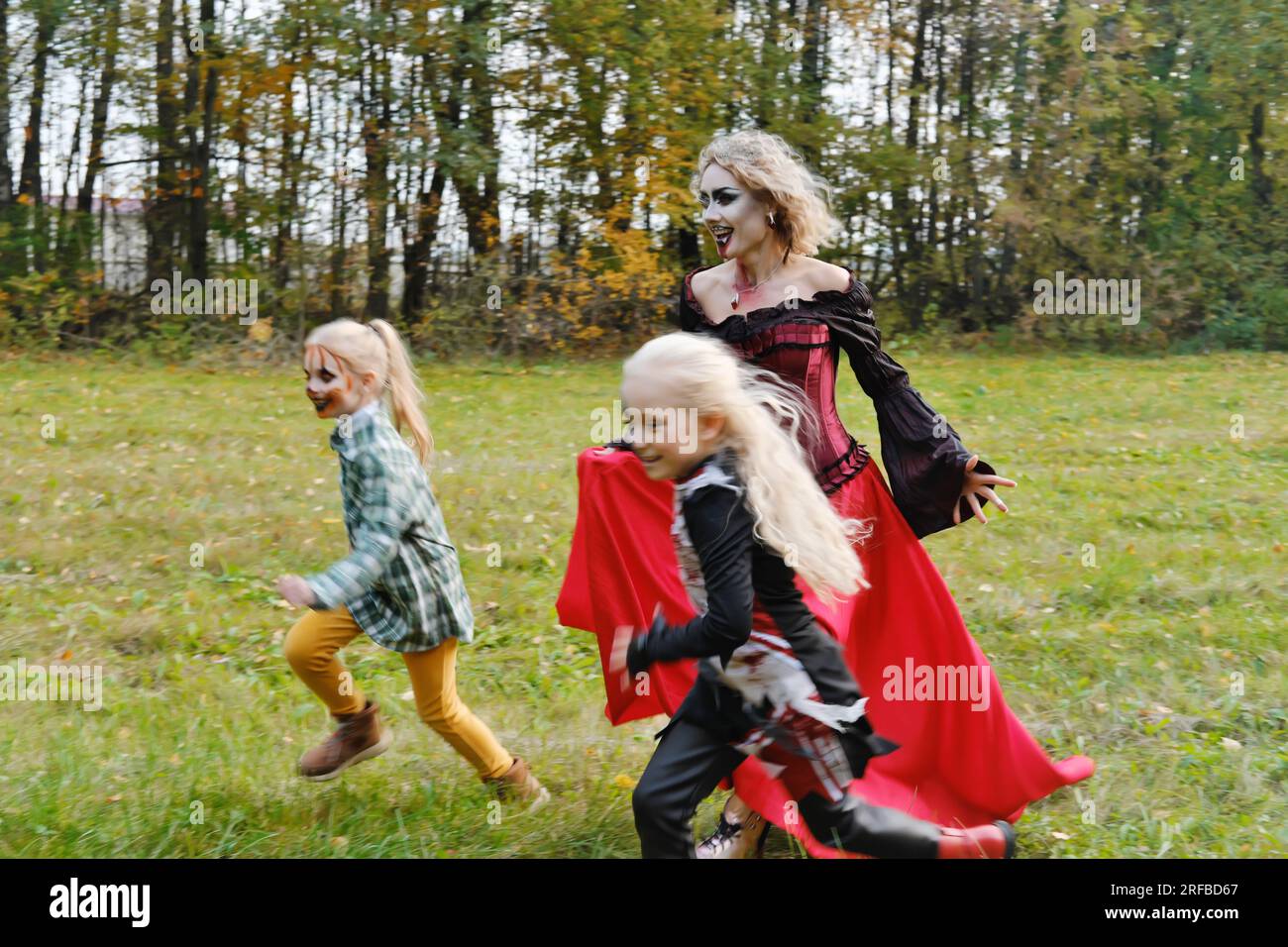 Die Familie feiert Halloween. Mom in Form eines Vampirs, Mädchen in Form einer Cheerleaderin und eines Kürbis. Mom spielt mit ihren Töchtern. Horizont Stockfoto
