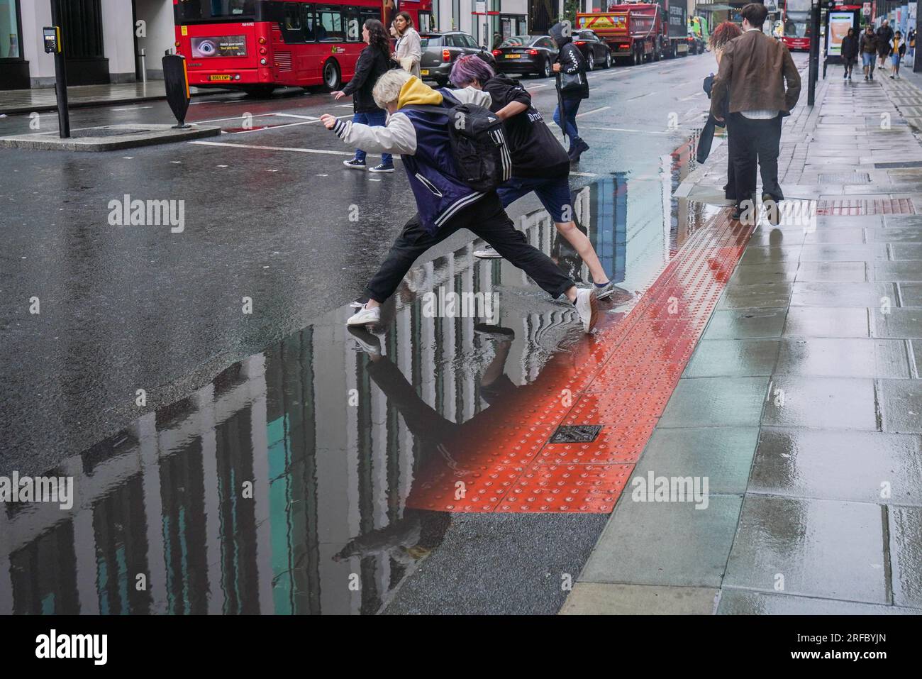 London UK. 2. August 2023 Fußgänger springen über einen großen Wassersee in einem regnerischen und stürmischen Londoner Büro, während das MET-Büro gelbe Warnungen für starke Winde in Großbritannien ausgibt. Kredit: amer Ghazzal/Alamy Live News Stockfoto