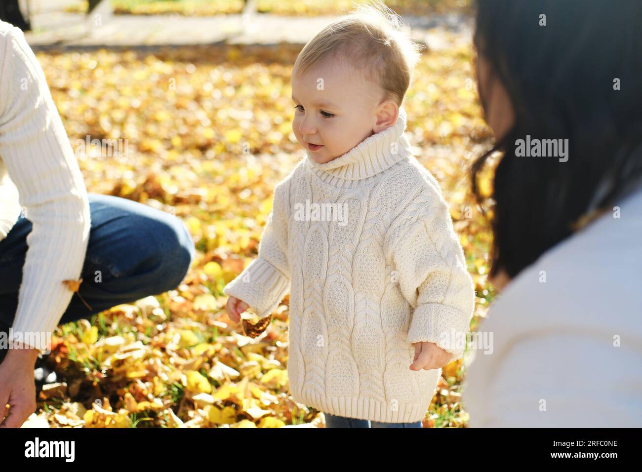 Familien und verbringen Zeit im Herbstpark bei sonnigem Wetter. Eltern schauen sich ihren kleinen Sohn an. Horizontales Foto Stockfoto
