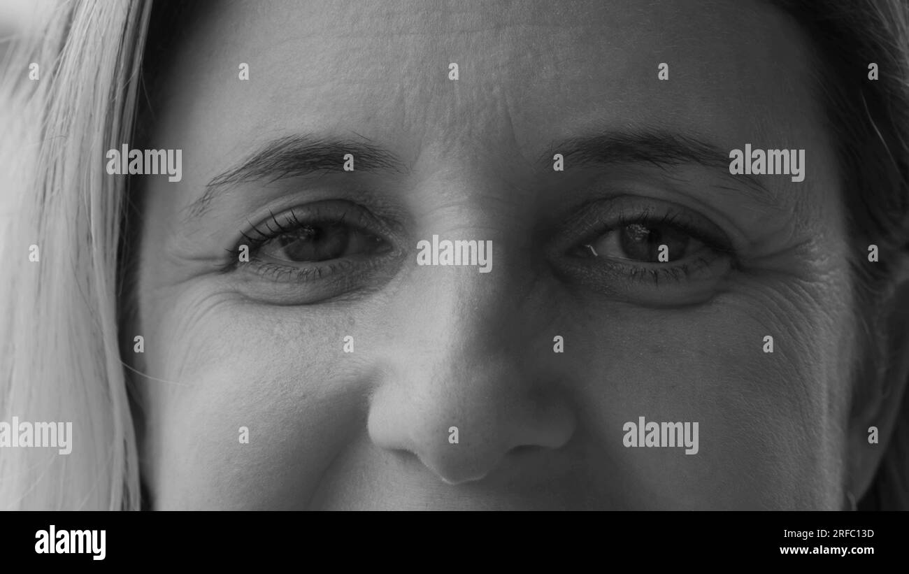 Makrodichte Nahaufnahme einer Frau in 40s, die in Schwarz-Weiß-Fotografie vor der Kamera lächelt. Monochromatischer Mensch, fröhlicher Ausdruck Stockfoto
