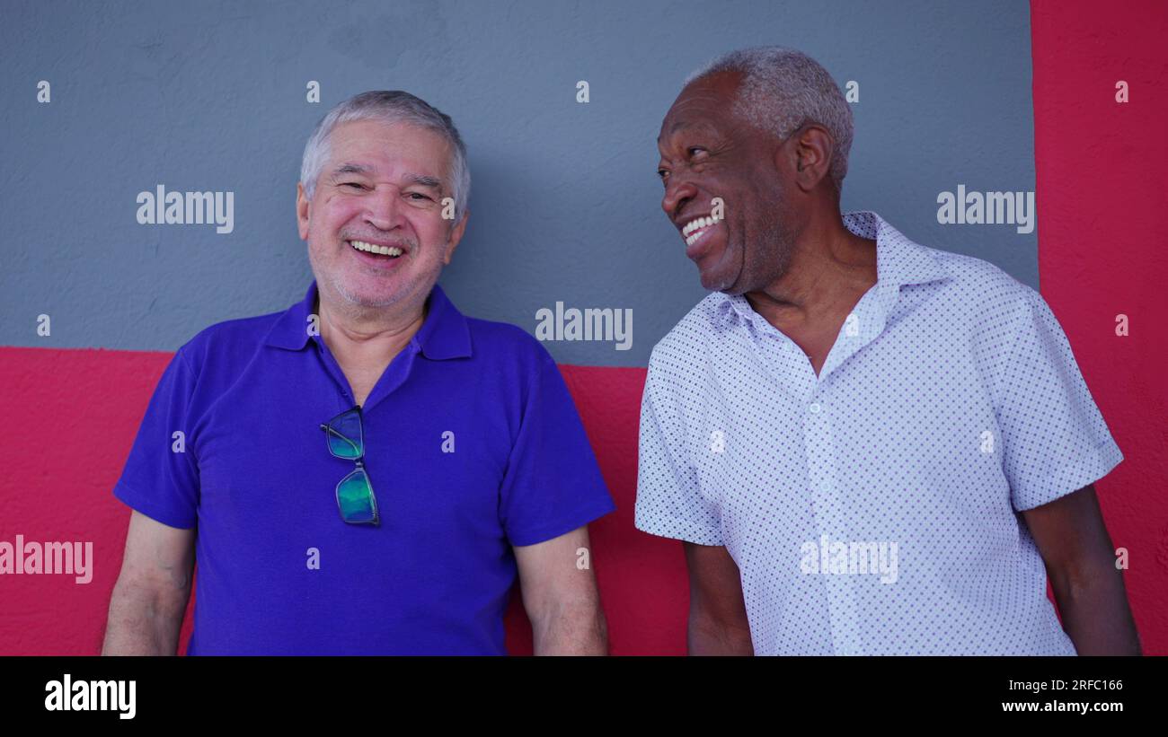 Alte Freundschaft von zwei verschiedenen Senioren, die auf der Straße stehen und lächeln, während sie miteinander interagieren Stockfoto