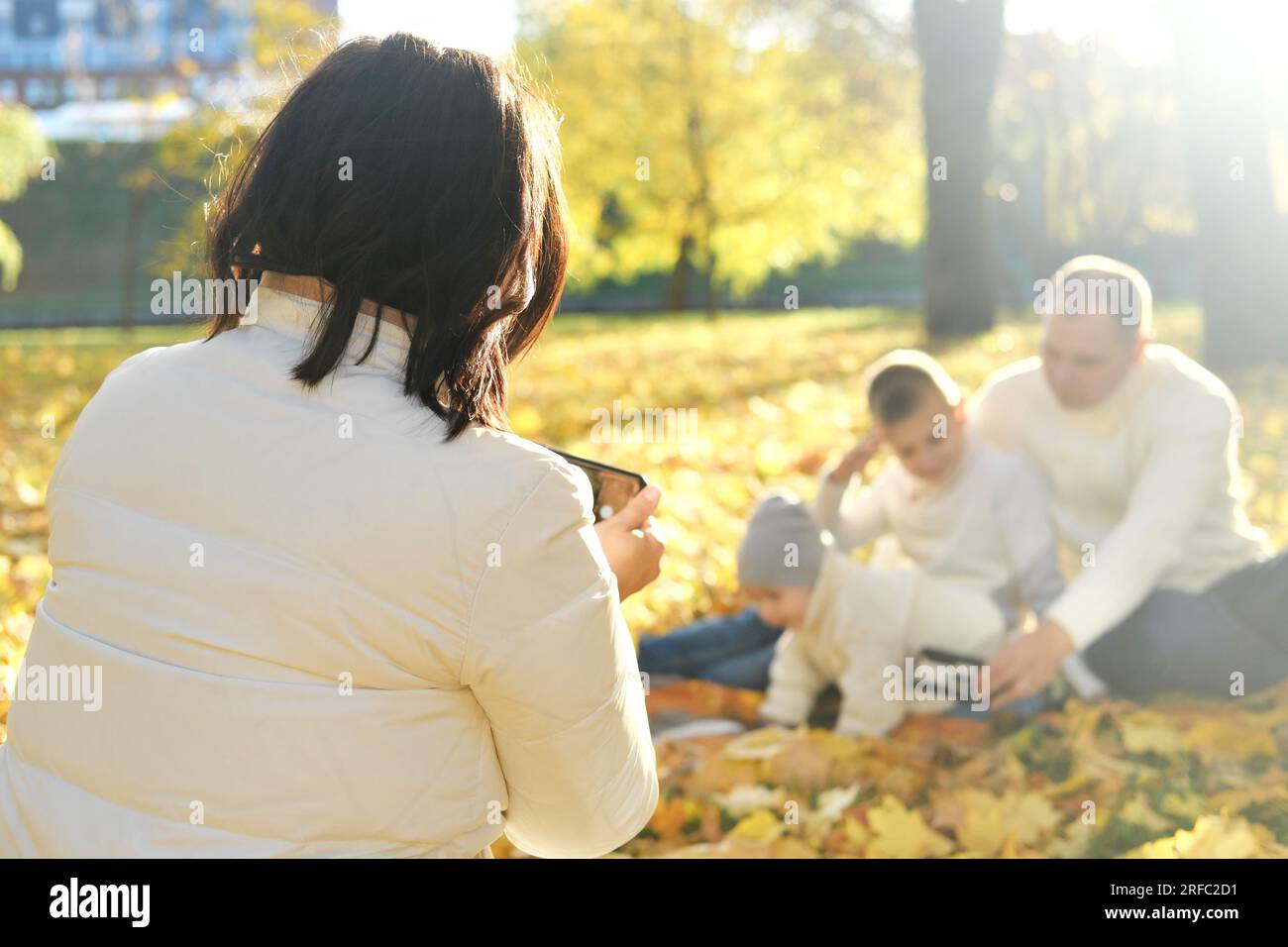 Eine glückliche vierköpfige Familie verbringt Zeit im Herbstpark. Mutter macht Fotos von ihrer Familie oder nimmt Videos auf dem Mobiltelefon auf. Horizontales Foto Stockfoto
