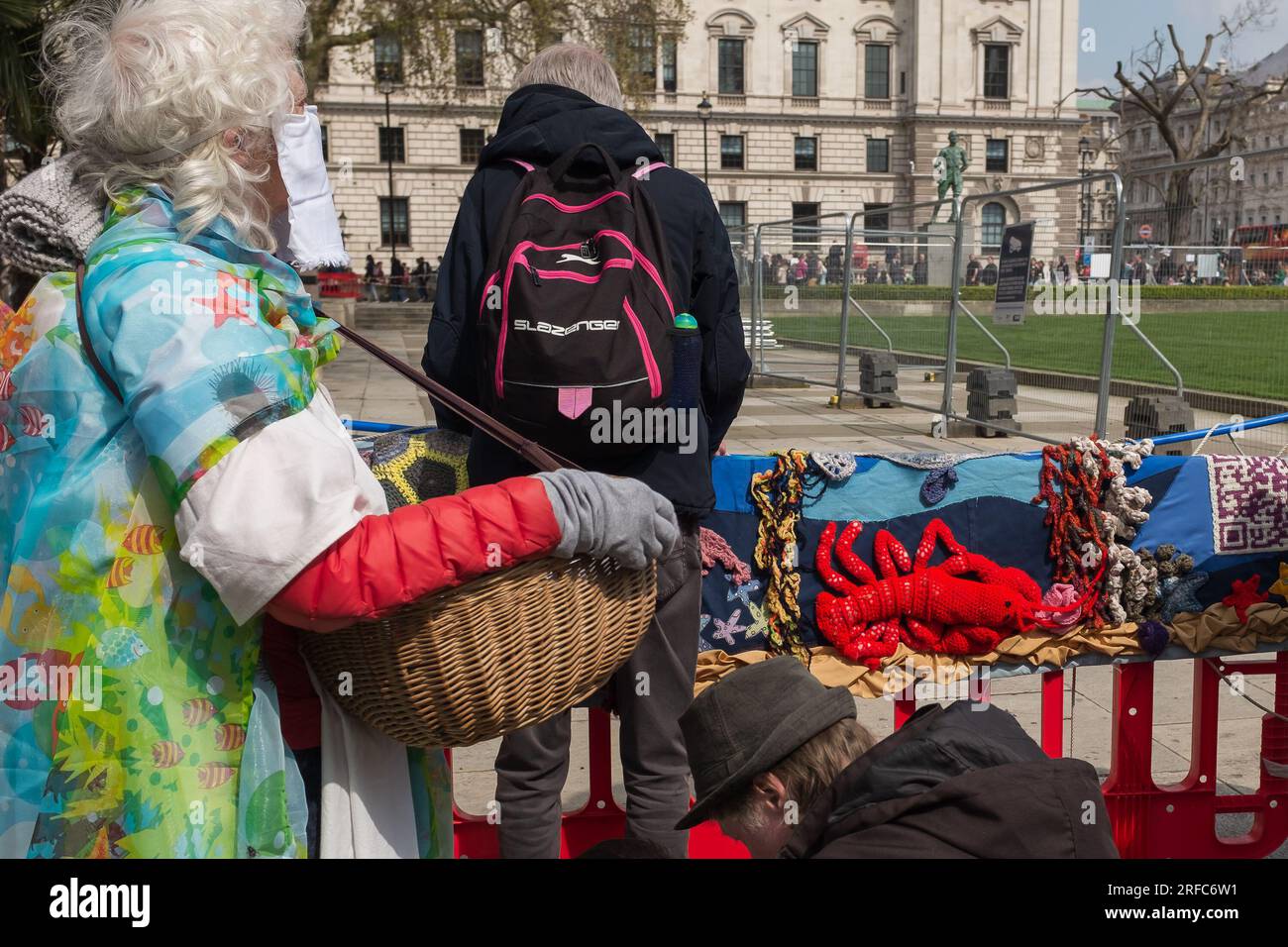 London, Großbritannien, 2023. Am Earth Day steht ein sehr farbenfroher Aktivist mit einem Korb vor einer erstaunlichen gestrickten Meereslandschaft mit einem großen roten Hummer Stockfoto