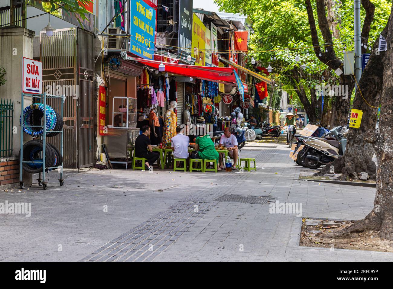 Hanoi, Vietnam - 28. Mai 2023: Eine lebendige Straße lädt zum Leben ein, wenn sich die Einheimischen in einem belebten Restaurant am Straßenrand versammeln. Sie sitzen auf niedrigen Hockern und lachen gemeinsam Stockfoto