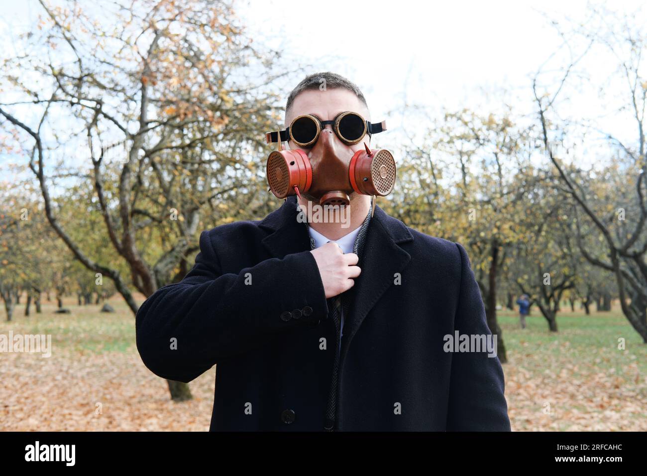 Ein Mann in schwarzem Mantel, Geschäftsanzug und Gasmaske, der im Herbstpark posiert. Horizontales Foto Stockfoto
