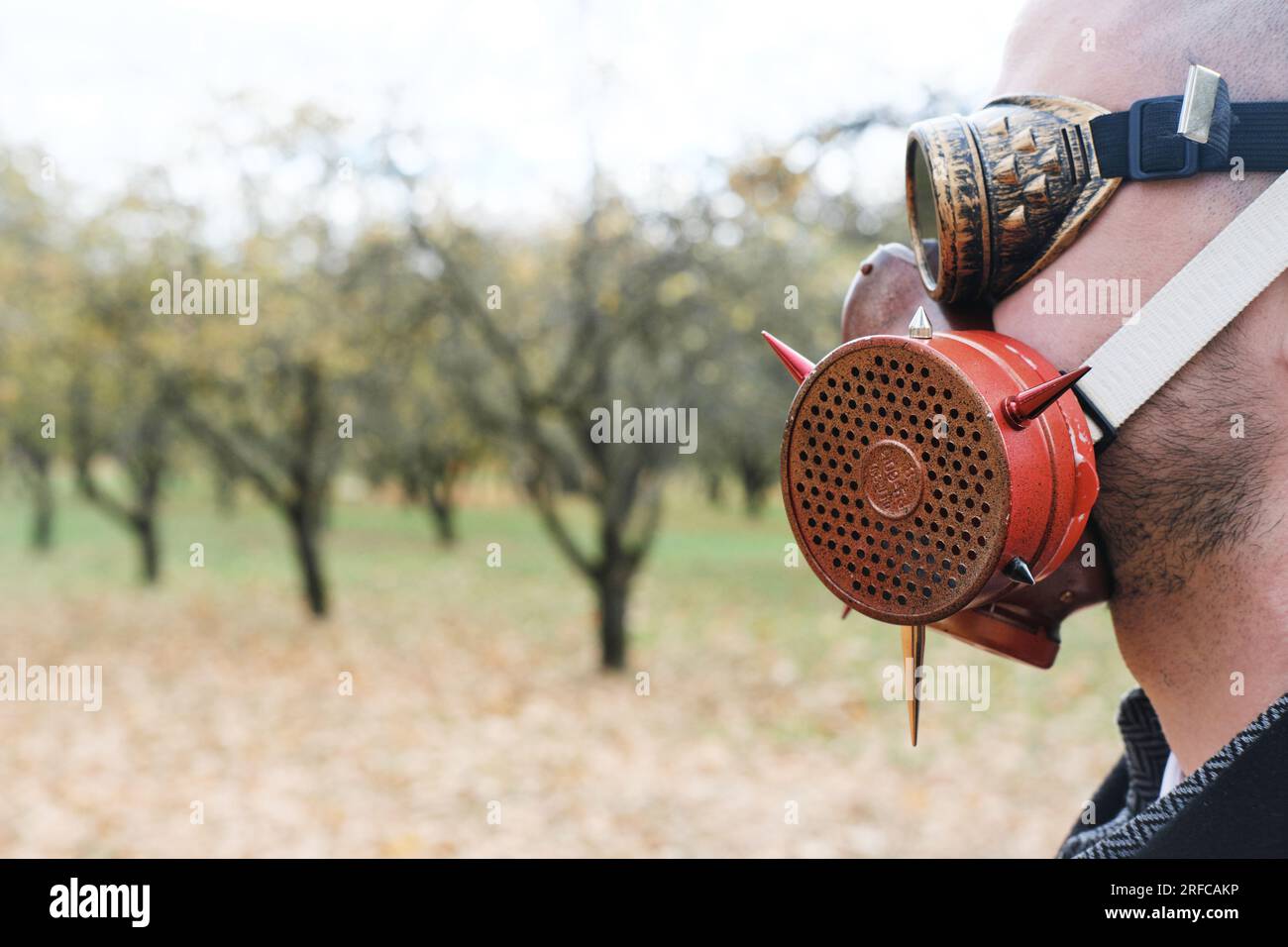 Ein Mann mit schwarzem Mantel, Business-Anzug, Gasmaske und Steampunk-Schutzbrille posiert in einem Herbstpark. Horizontales Foto Stockfoto