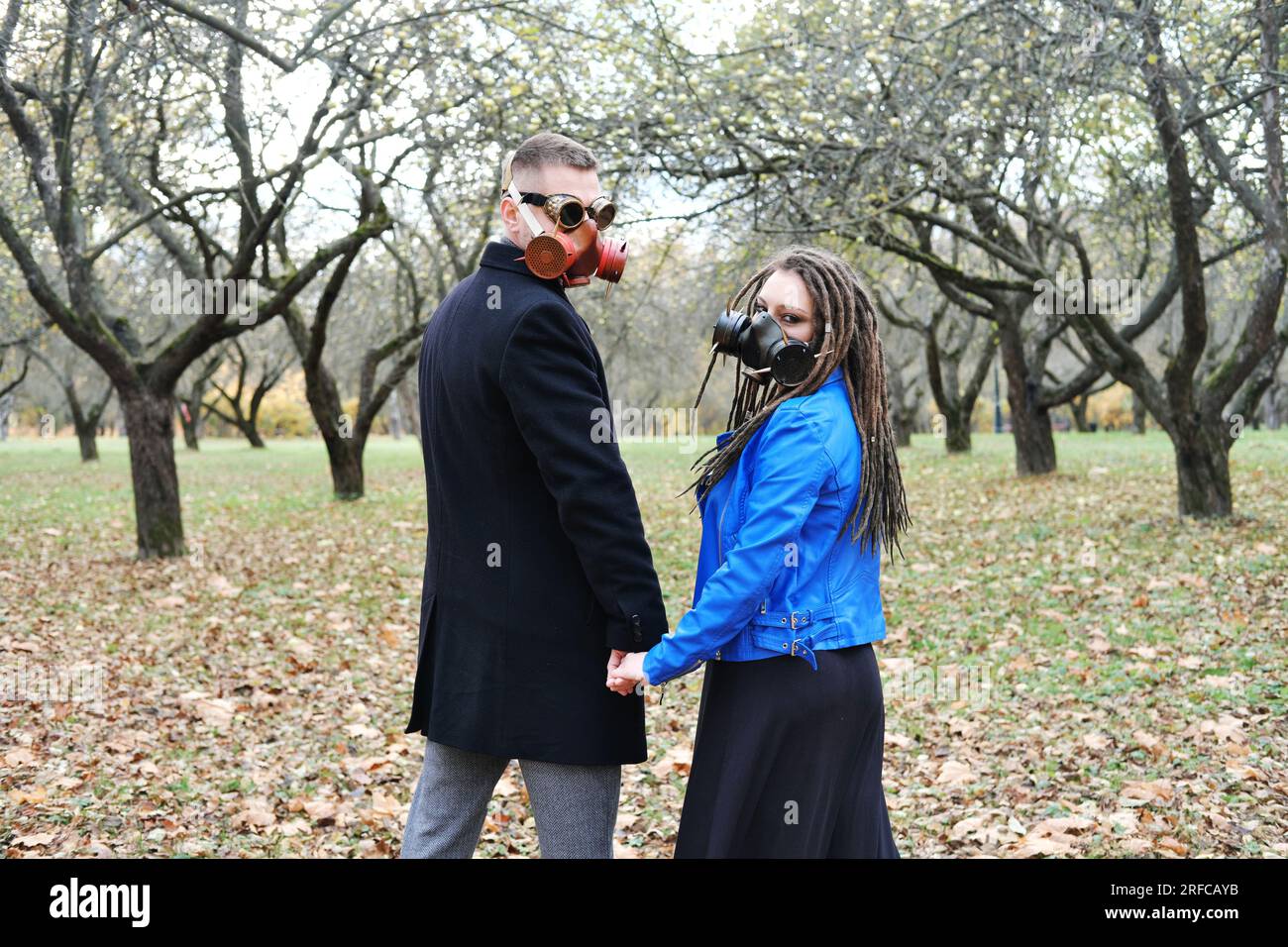Eine Frau mit Dreadlocks und einer Gasmaske hält die Hand eines Mannes mit einer Steampunk-Brille und einer Gasmaske. Liebe in einer ökologischen Katastrophe. Horizontales Foto Stockfoto