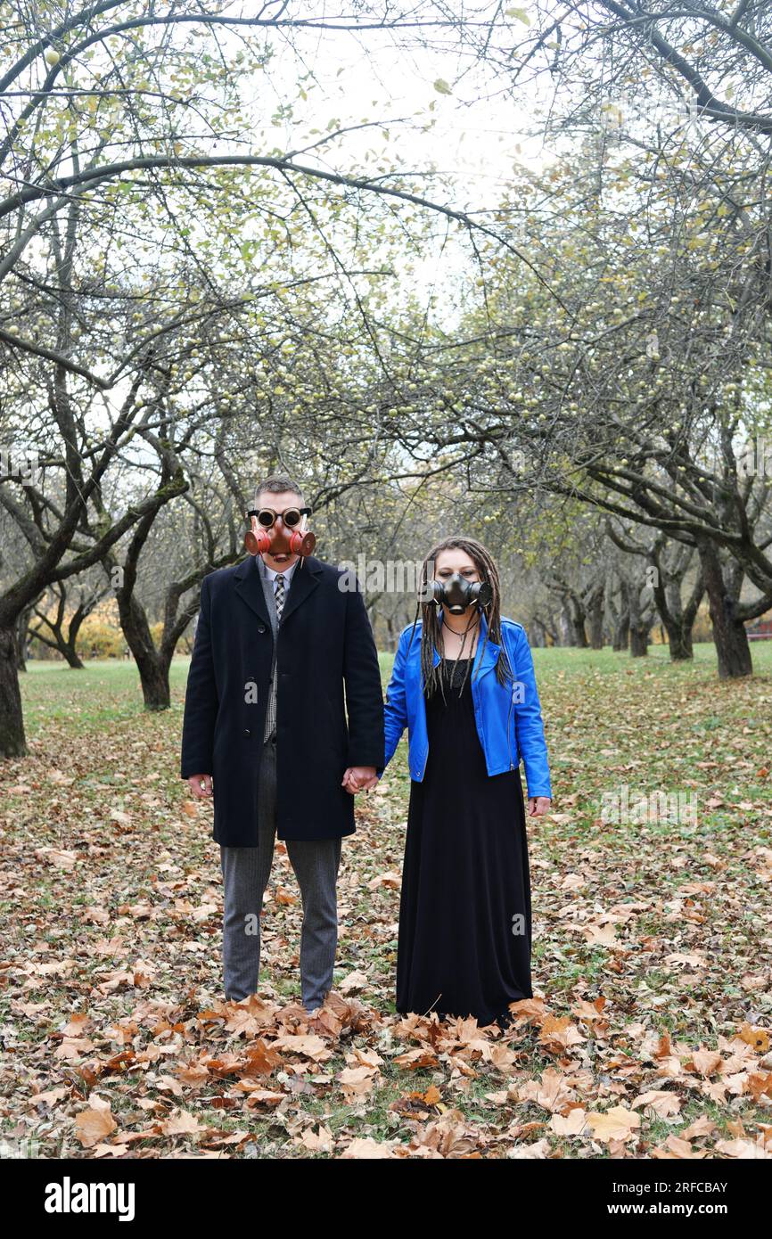 Mann und Frau in Gasmasken halten Händchen und posieren im Herbstpark. Der Mann trägt eine Steampunk-Schutzbrille. Vertikales Foto Stockfoto