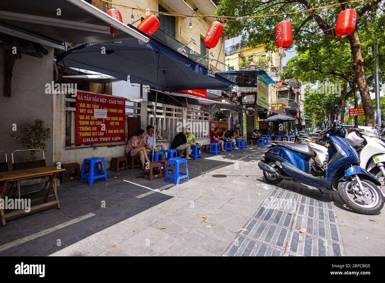 Hanoi, Vietnam - 28. Mai 2023: Eine lebendige Straße lädt zum Leben ein, wenn sich die Einheimischen in einem belebten Restaurant am Straßenrand versammeln. Sie sitzen auf niedrigen Hockern und lachen gemeinsam Stockfoto